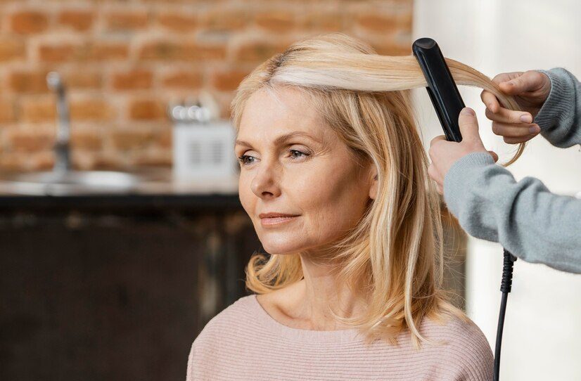mature woman getting her hair straightened by hairdresser home_23 2148817236 e1739974922383